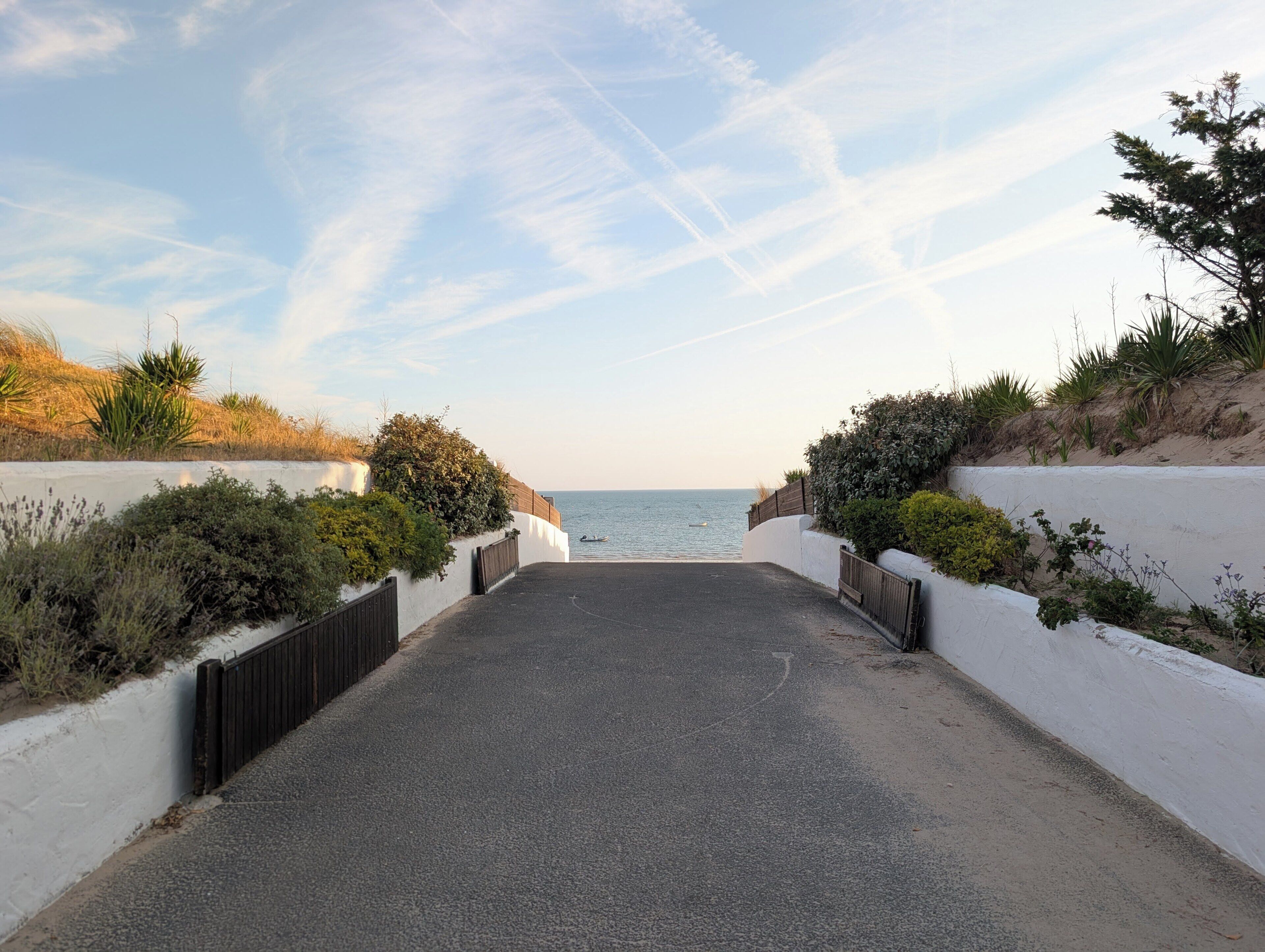 A paved pathway leading to a body of water, flanked by white walls and greenery.