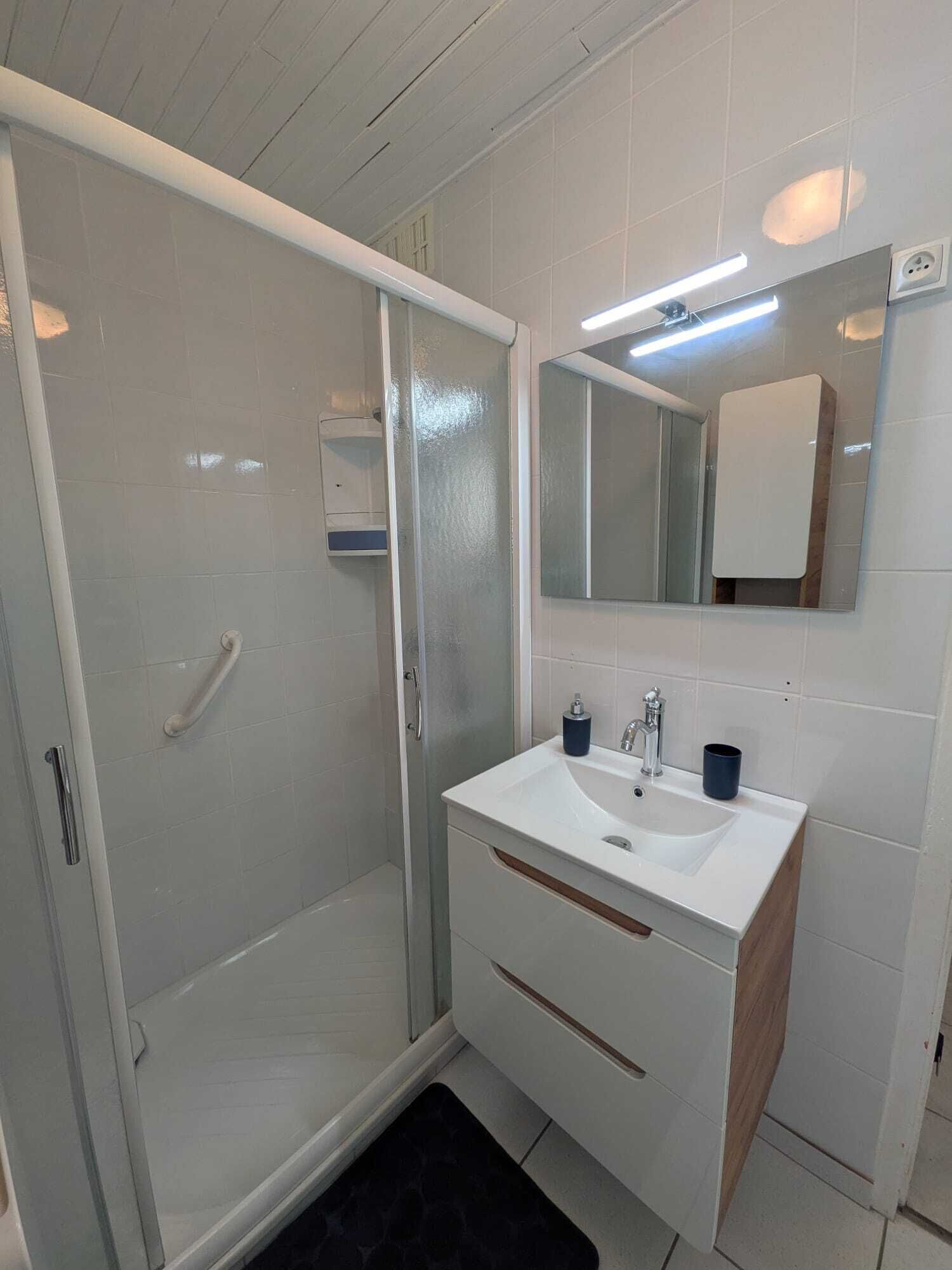 A modern bathroom with a glass shower enclosure, a white sink with a mirror above it, and a wooden vanity.