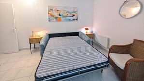 Un dormitorio con cama, una silla, mesita de noche con lámpara, espejo en la pared y un cuadro.