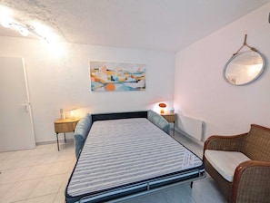 A bedroom with a bed, a chair, a bedside table with a lamp, a wall-mounted mirror, and a painting. - N0 Apt, 3-star rated, GF & 200 m² garden, 150 m from the beach – La Guérinière (La Guérinière)