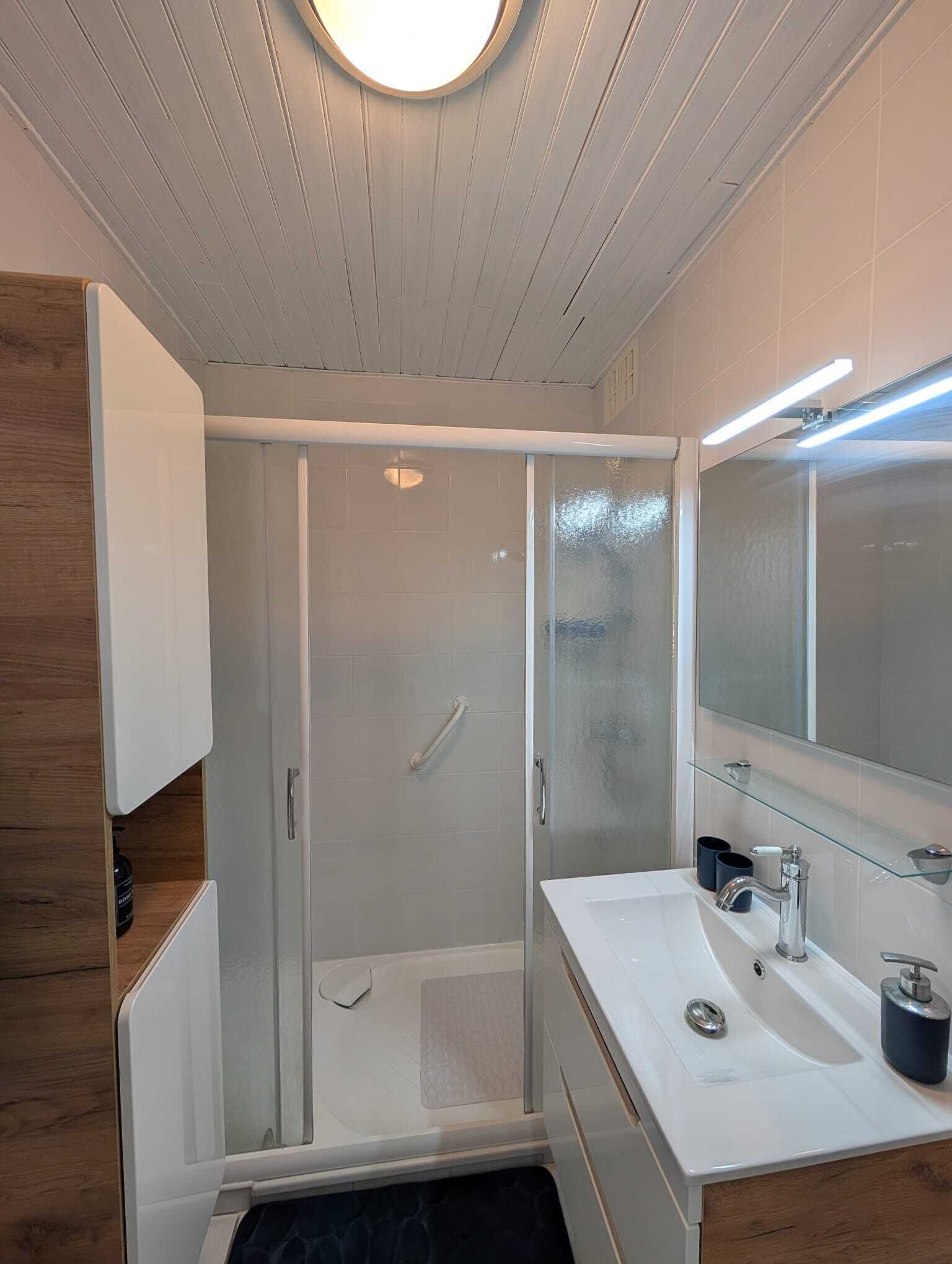A modern bathroom with a glass shower enclosure, a white sink with a mirror, and a wooden vanity.