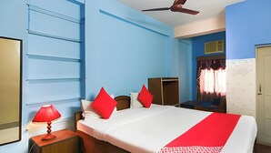 Une chambre d’hôtel avec un lit, une table de chevet, un ventilateur de plafond et une fenêtre avec des rideaux.