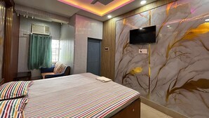 Une chambre avec un lit, une télévision, un ventilateur de plafond et un mur décoré d’un motif représentant un arbre.