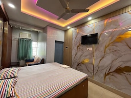 Un dormitorio con cama, televisor, ventilador de techo y una pared decorada con un diseño de árbol.