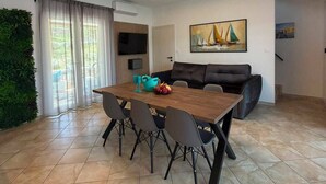 Un soggiorno moderno con zona pranzo, un divano nero, un quadro e un'ampia finestra con tende.
