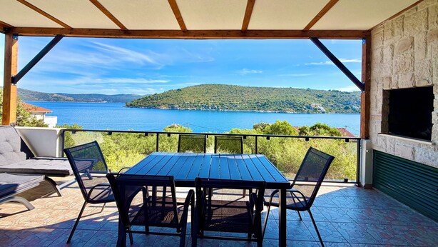 Un’area relax all’aperto, riparata, con tavolo e sedie, affacciata su uno specchio d’acqua e un paesaggio collinare.