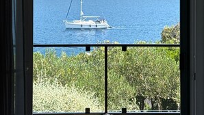 Una finestra con vista su un'acqua calma, una barca a vela e un paesaggio collinare.