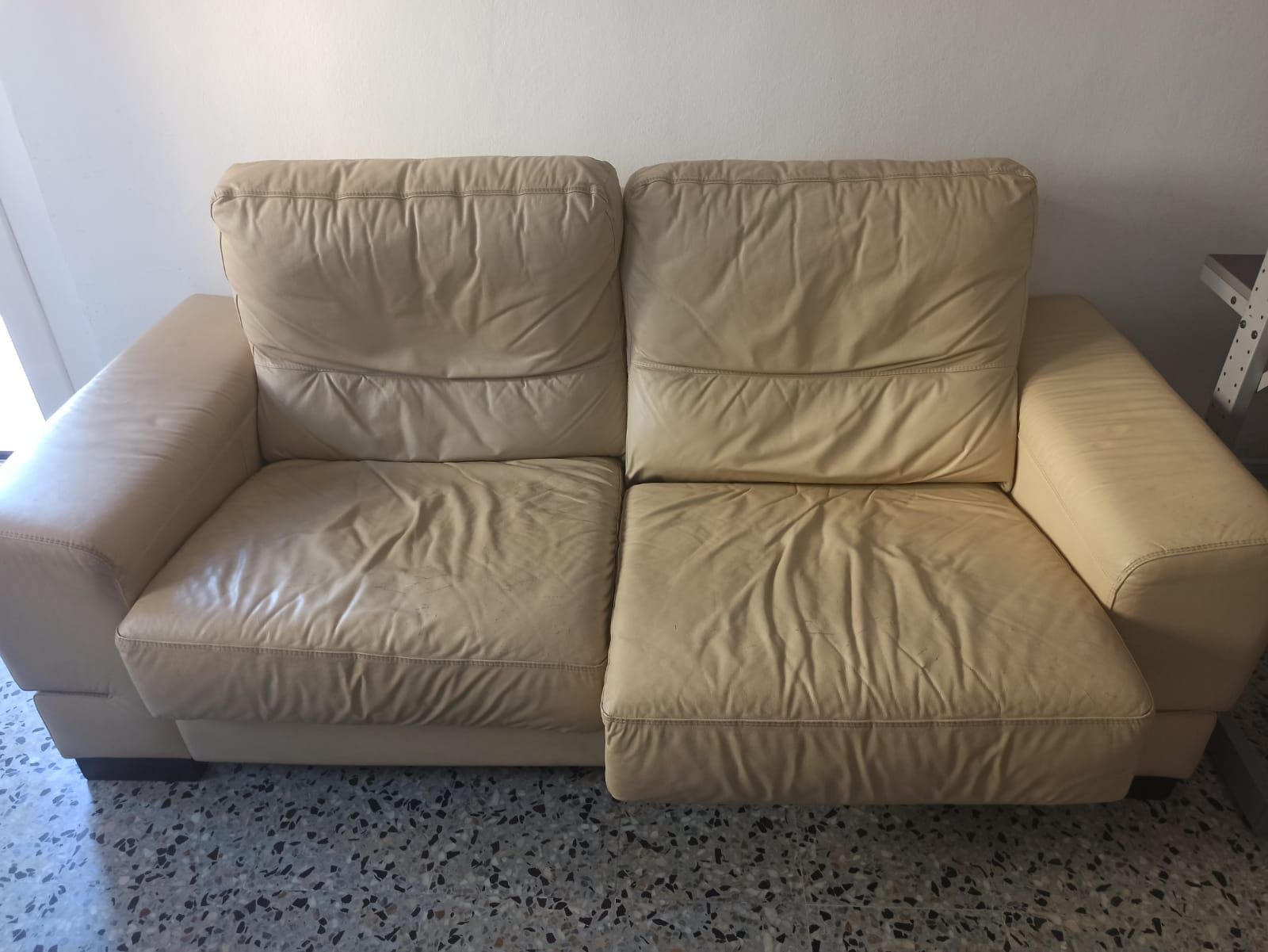 A beige leather sofa with a simple design, positioned against a wall with a speckled floor.