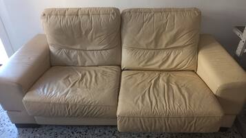 A beige leather sofa with a simple design, positioned against a wall with a speckled floor.