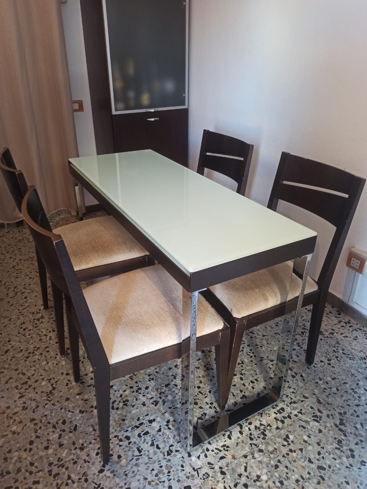 A dining area with a rectangular table, four chairs, and a glass partition.