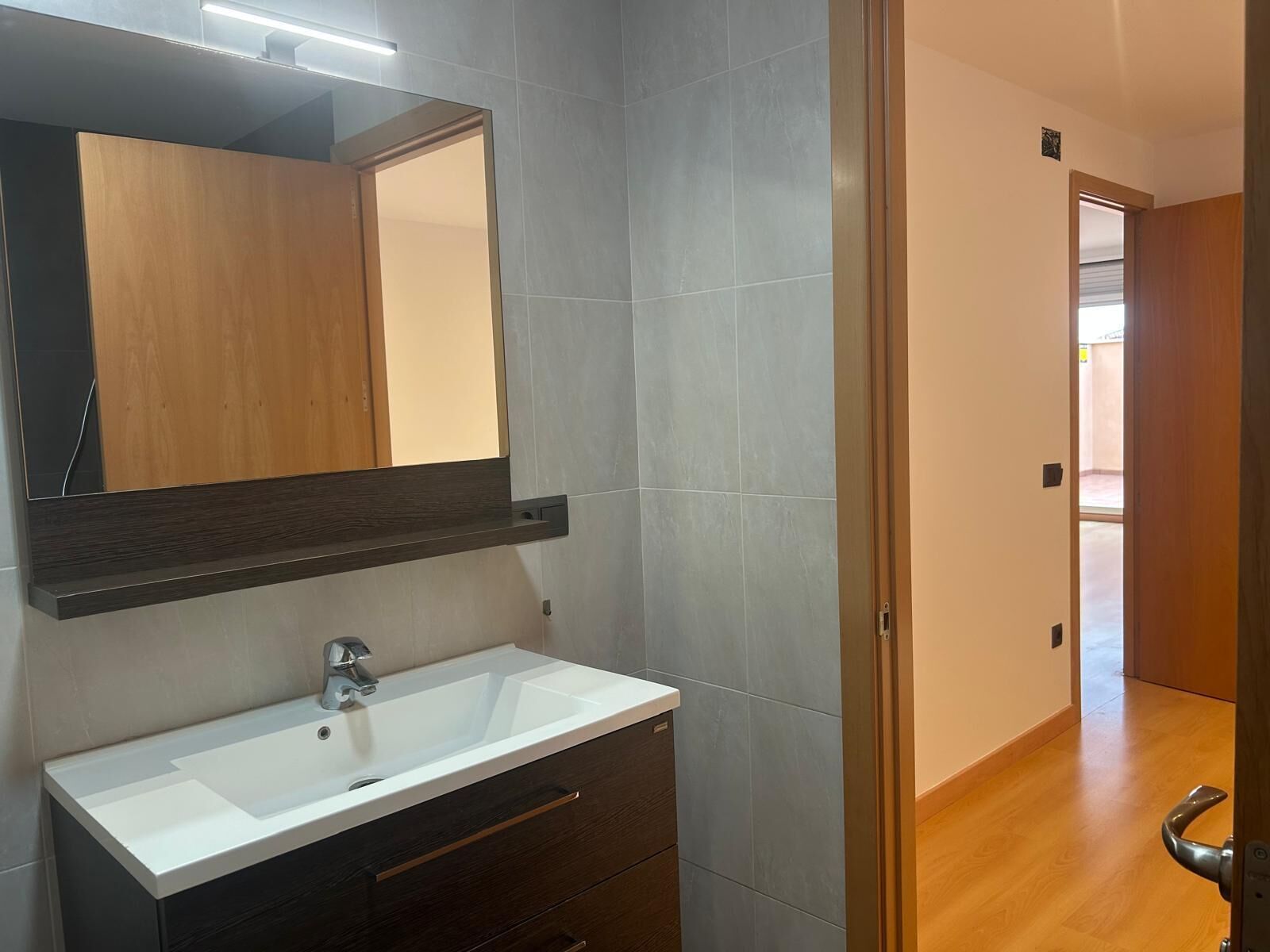 A bathroom with a white sink, dark wood vanity, and a mirror with a wooden frame.