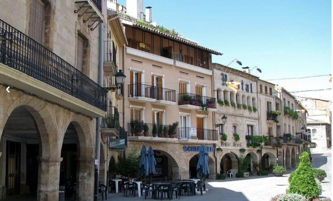 Un edificio con varios balcones, mobiliario exterior y un letrero que dice 'SCHINER'.