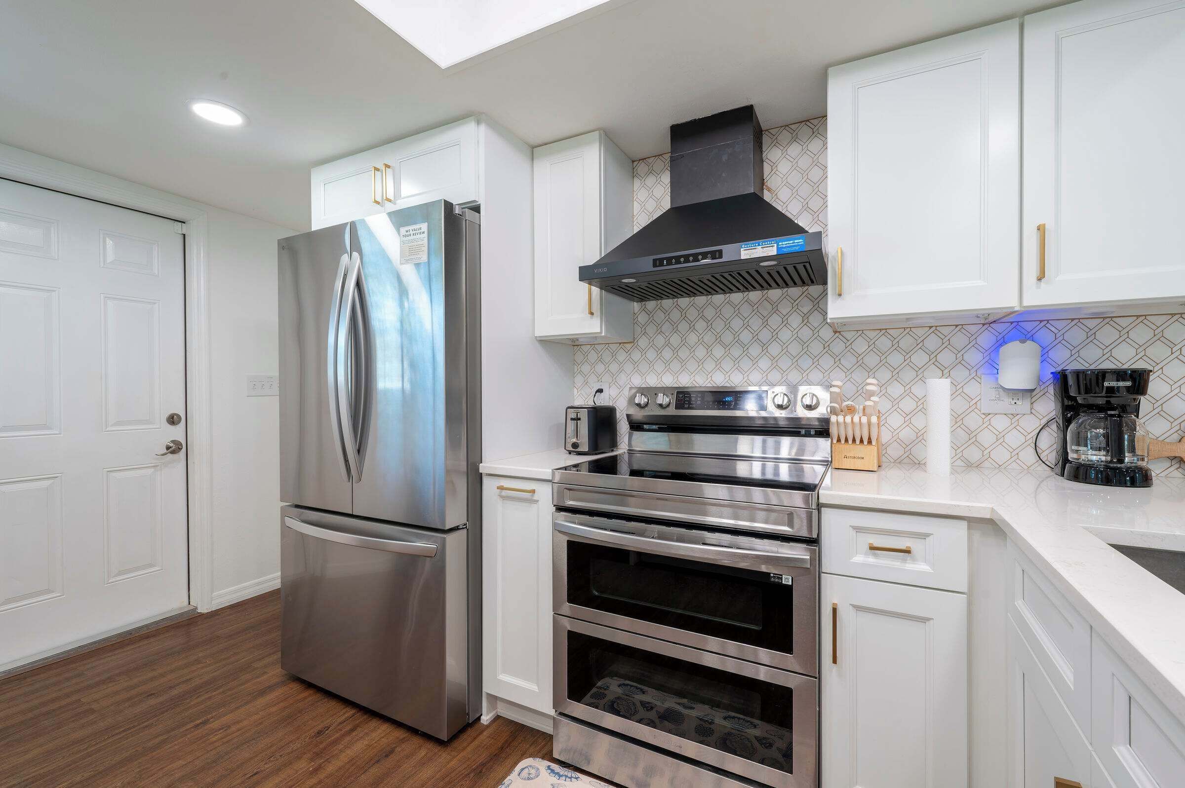 A modern kitchen with stainless steel appliances, white cabinetry, and a patterned backsplash.