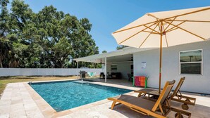 A swimming pool with lounge chairs and an umbrella, surrounded by a patio area. - Seminole Family Escape: Pool, Games & BBQ (Seminole)