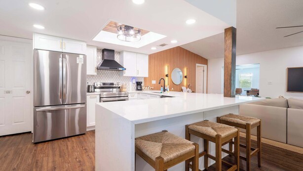 A modern kitchen with a stainless steel refrigerator, wooden cabinets, a large island with bar stools, and recessed ceiling lighting. - Seminole Family Escape: Pool, Games & BBQ (Seminole)