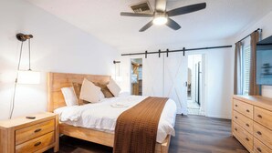 A bedroom with a bed, wooden nightstand, dresser, ceiling fan, and a view of the outside. - Seminole Family Escape: Pool, Games & BBQ (Seminole)