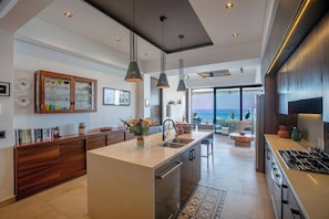 A modern kitchen with a central island, pendant lighting, and a view of the ocean. - Oceanview 2BR | BBQ Terrace & Rooftop Pool (Puerto Vallarta)