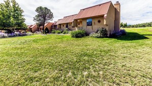 A two-story building with a red-tiled roof, surrounded by a well-maintained lawn and flowering plants. - Aspen Run Condo Unit 29A | Great Views & Location! (Ruidoso)