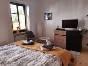 A bedroom with a bed, a chair, a small table, a dresser, a TV, and a window with blinds. - Vacation Rental T19-Dresden (Dresden)