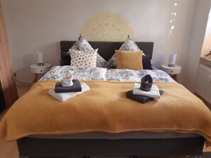 Ein ordentlich bezogenes Bett mit einer gemusterten Tagesdecke, zwei Kissen und zwei gefalteten Handtüchern.