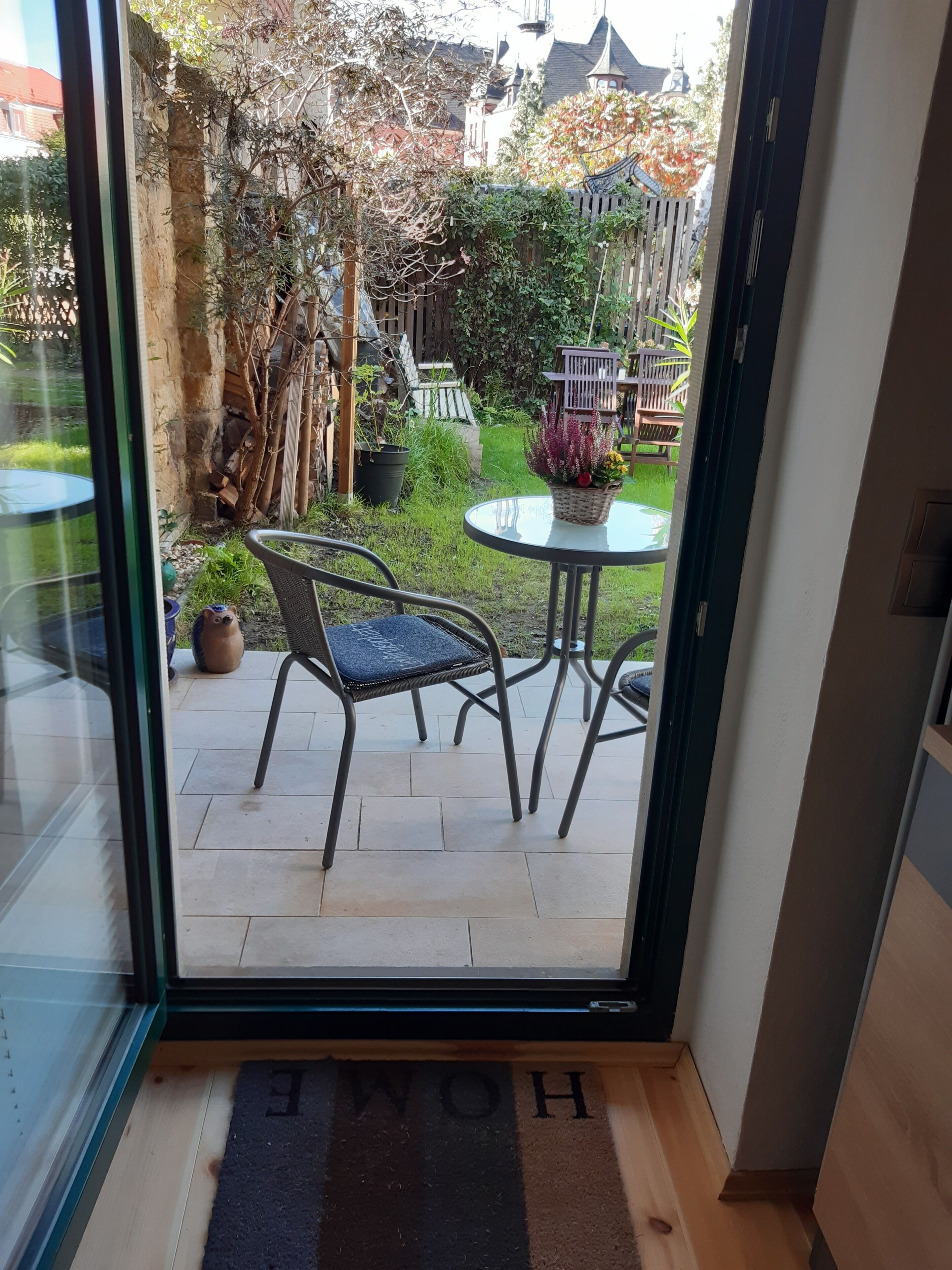 A glass door leading to a patio with a chair, a small round table, and a doormat with 'HOME' written on it.
