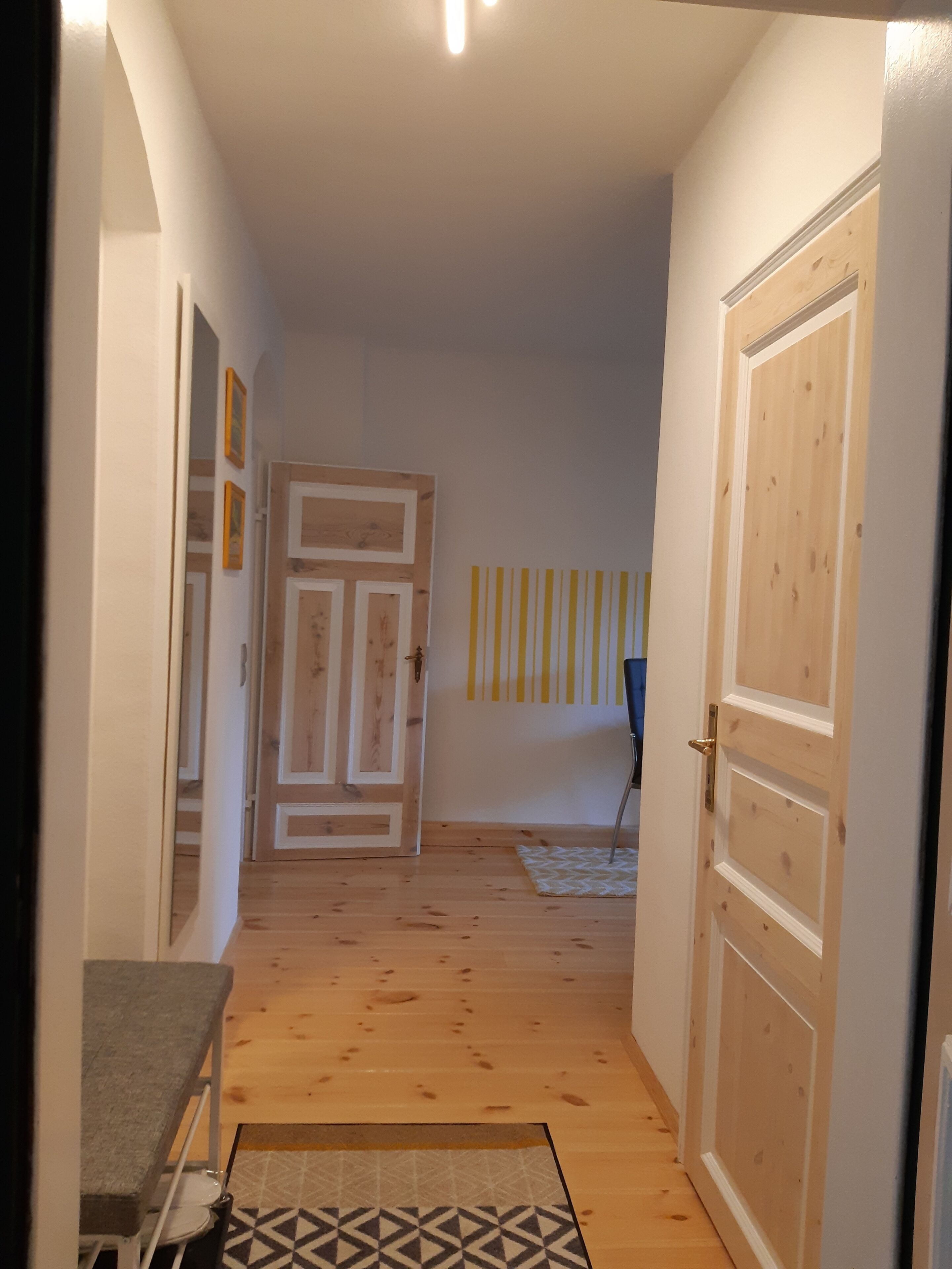 A hallway with wooden flooring, a door on the right, and a wall with vertical lines.