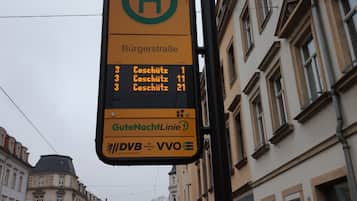 Ein Bushaltestellenschild mit Streckeninformationen und einer digitalen Anzeige, die Ankunftszeiten von Bussen zeigt.