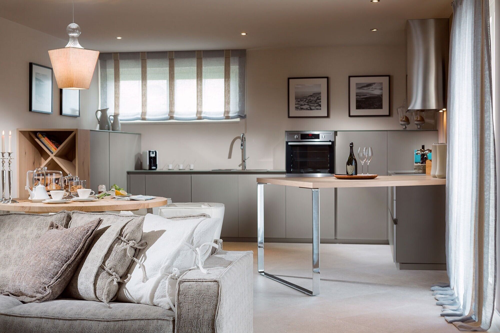 A modern kitchen with a central island, a dining area with a sofa, and a large window with curtains.