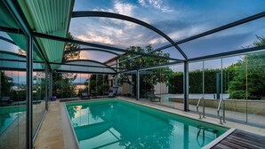 A swimming pool with a glass enclosure, a wooden deck, and a view of the surrounding landscape.