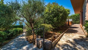 A stone pathway leading to a building with a covered entrance, surrounded by greenery and trees.