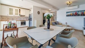 A modern kitchen with white cabinets, a dining area with a marble table, and a living space with a sofa and a painting.