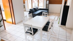 Un intérieur moderne avec une table à manger blanche, des chaises blanches, un canapé foncé et un meuble blanc.