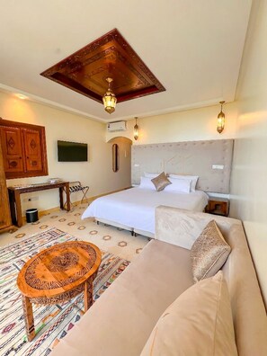 Habitación de hotel con cama, sofá, escritorio, televisor y techo con diseño decorativo.