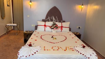 Een hotelkamer met een bed versierd met rozenblaadjes en een hartvormige bloemenopstelling waarop 'LIEFDE' staat.