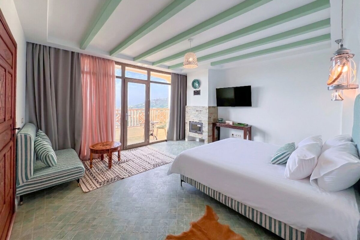 A hotel room with a bed, a TV, a small table, a sofa, and a view of the outdoors.