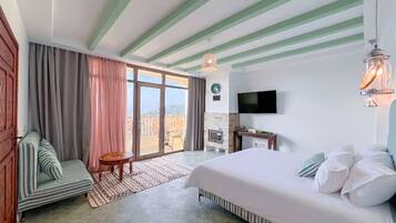 A hotel room with a bed, a TV, a small table, a sofa, and a view of the outdoors.