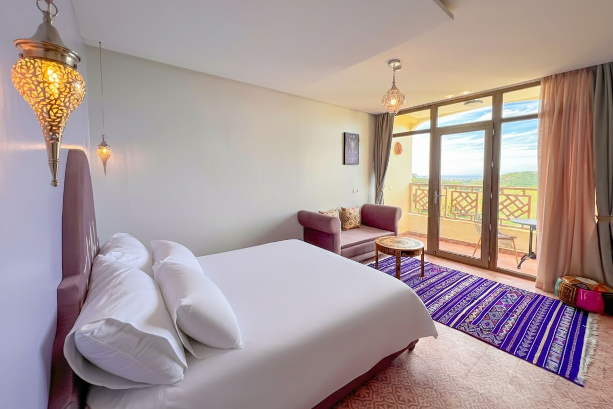 A hotel room with a bed, a sofa, a small table, and a balcony with a view.