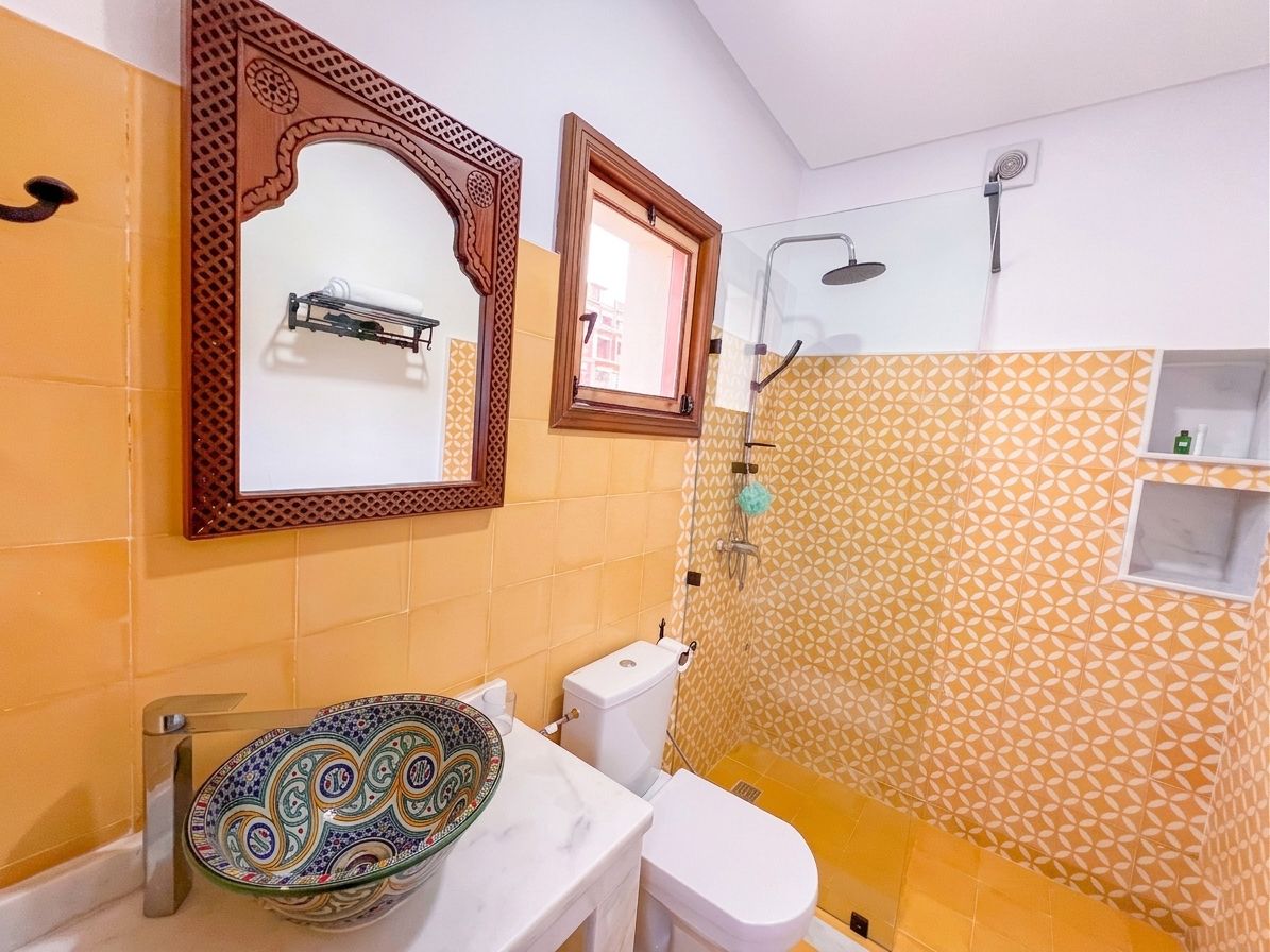 A bathroom with a toilet, a sink with a decorative bowl, a shower area, and patterned walls.