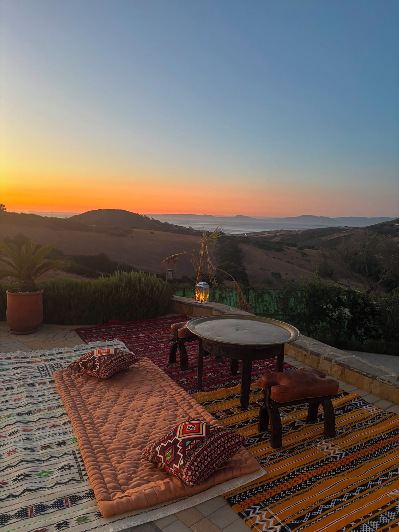 Una terraza con una mesa redonda y sillas, una alfombra estampada y vistas del paisaje.
