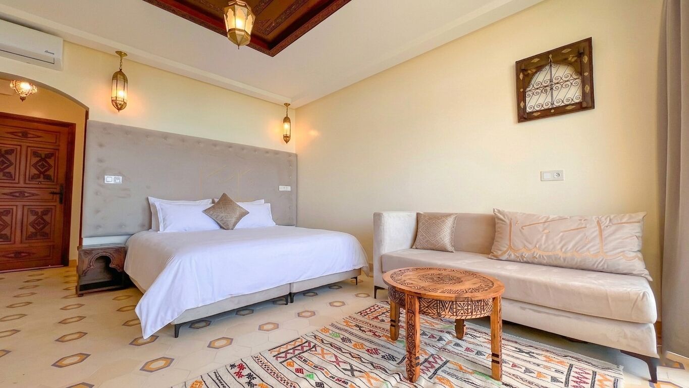 A bedroom with a bed, a sofa, a small round table, and a patterned rug.