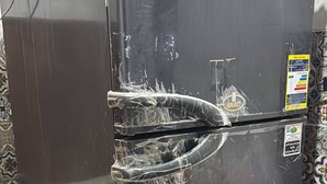 Ein schwarzer Kühlschrank mit beschädigter Tür und einem Aufkleber an der Seite.