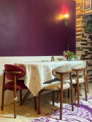 A dining area with a table set for four, a purple wall, and a brick accent wall. - Pharaonic 2BR Apt Near Giza Pyramids GEM AC WiFi Balcony (Giza)