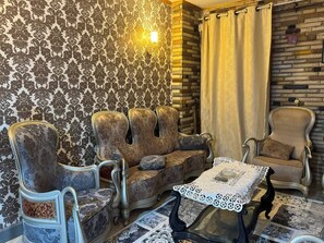 Uma sala de estar tradicional com papel de parede estampado, um sofá, duas poltronas, uma mesa de centro e uma cortina.