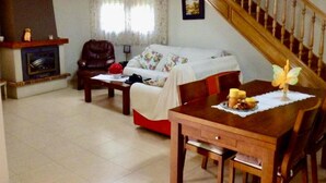 Ein Wohnzimmer mit einer Couch, einem Esstisch mit Stühlen, einem Kamin und einer Treppe.