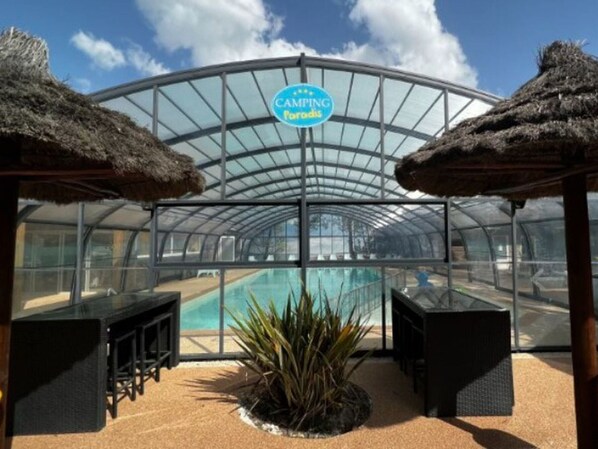 A glass-enclosed pool area with thatched umbrellas and seating. - Mobile home, pets welcome - 4 guests (Carcans)