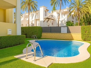 A swimming pool with a pool ladder, surrounded by well-maintained grass and palm trees, with a building in the background.