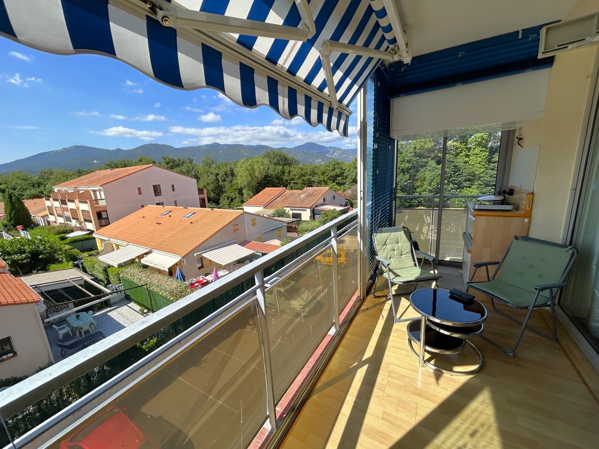 Un balcón con vistas a una zona residencial y montañas, amueblado con una mesa y sillas.