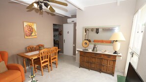 Ein Wohnzimmer mit Esstisch, Stühlen, einer Couch, einem Fernseher, einem Deckenventilator, einer Lampe und einem Spiegel.