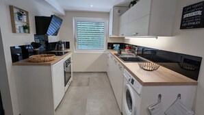 A compact kitchen with a washing machine, a sink, and a window with blinds. - Family Retreat with Terrace and Pool Access (Jeanménil)