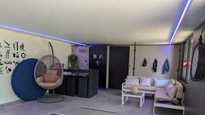A modern interior with a hanging chair, a sofa, a reception desk, and a wall with various icons. - Family Retreat with Terrace and Pool Access (Jeanménil)